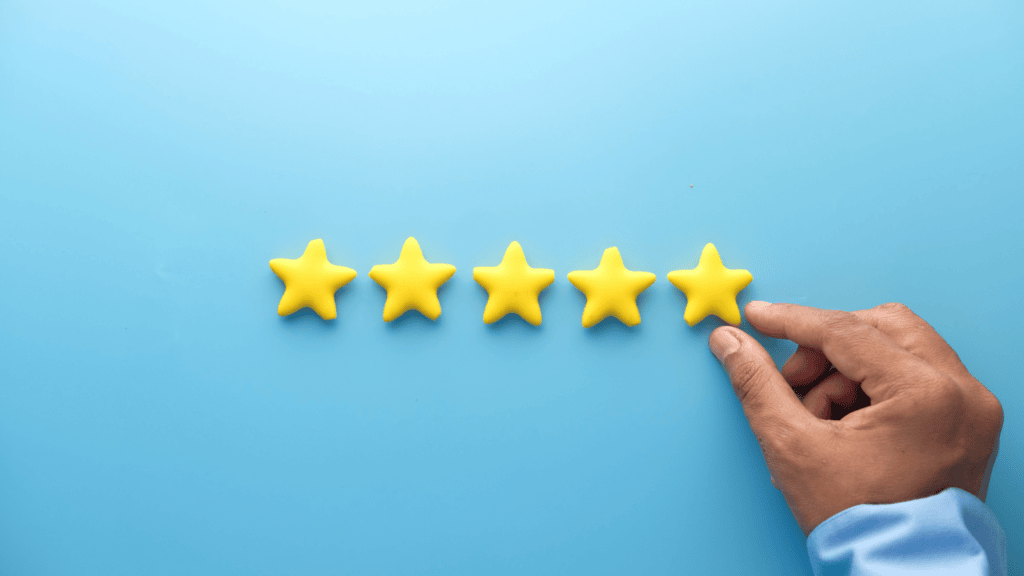 A man's hand touches 5 yellow stars, set against a blue background. Represents the concept of how to reply to negative reviews online.