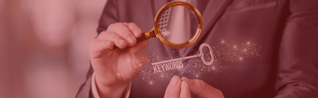 A man holds a magnifying glass up to a key with the teeth spelling "keyword" to symbolize the concept of finding the right SEO keyword research services. Image has a red tint, symbolic of the Digital Strike - Targeted Marketing brand.