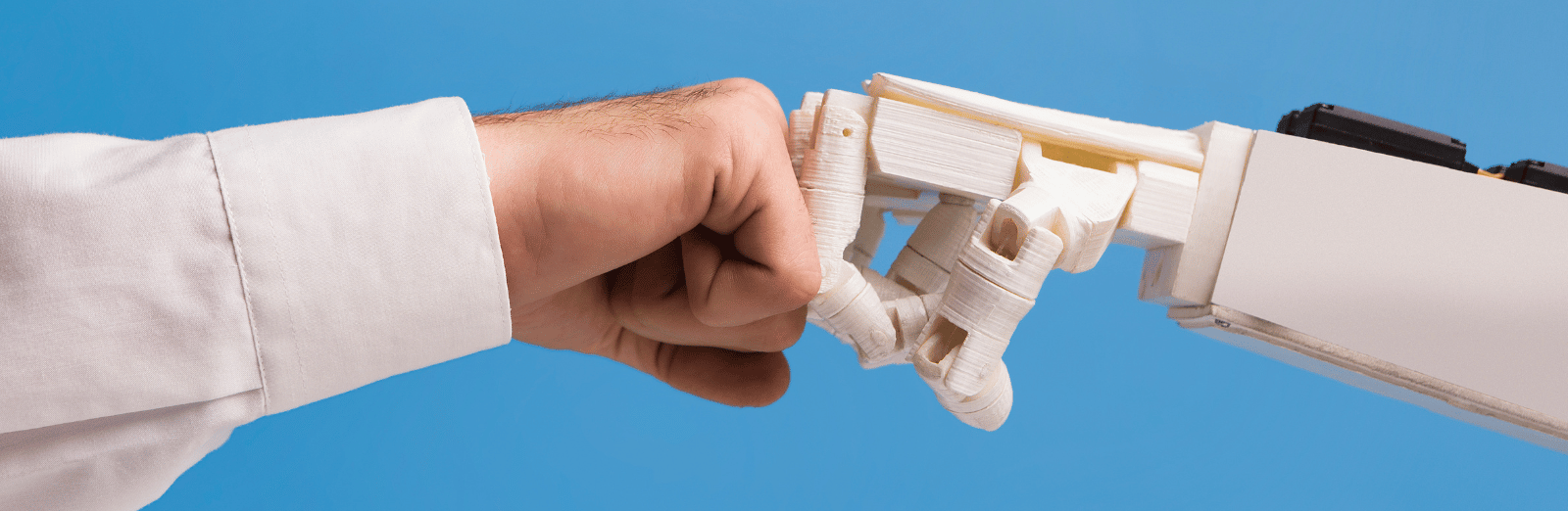A human fist bumps a robot arm, symbolizing the concept of human vs AI.