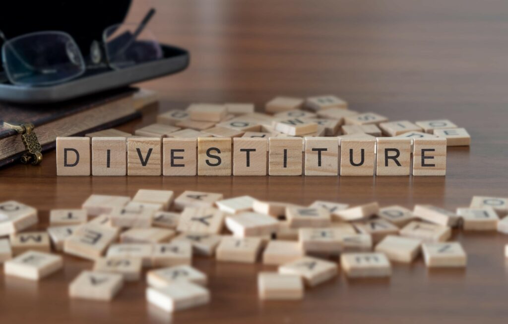 divestiture word or concept represented by wooden letter tiles on a wooden table with glasses and a book