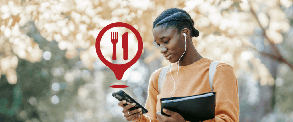 A young person at the park looks at their phone. A restaurant icon floats above the phone, representing the concept of geofencing marketing for a restaurant.