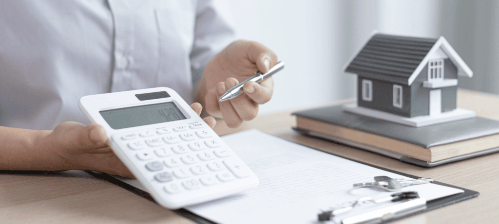 A mortgage lender shows a calculator, next to a miniature home, a book, a clipboard, and keys. Represents the concept of finding a mortgage lender for a new home.