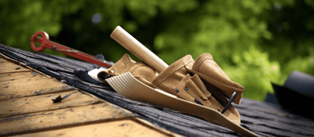 A roof with asphalt shingles. Roofer tools lay on the shingles. Trees in the background.