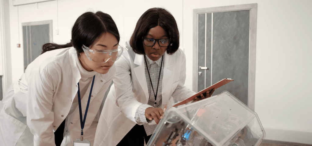 Two scientists examine an experiment and take notes.