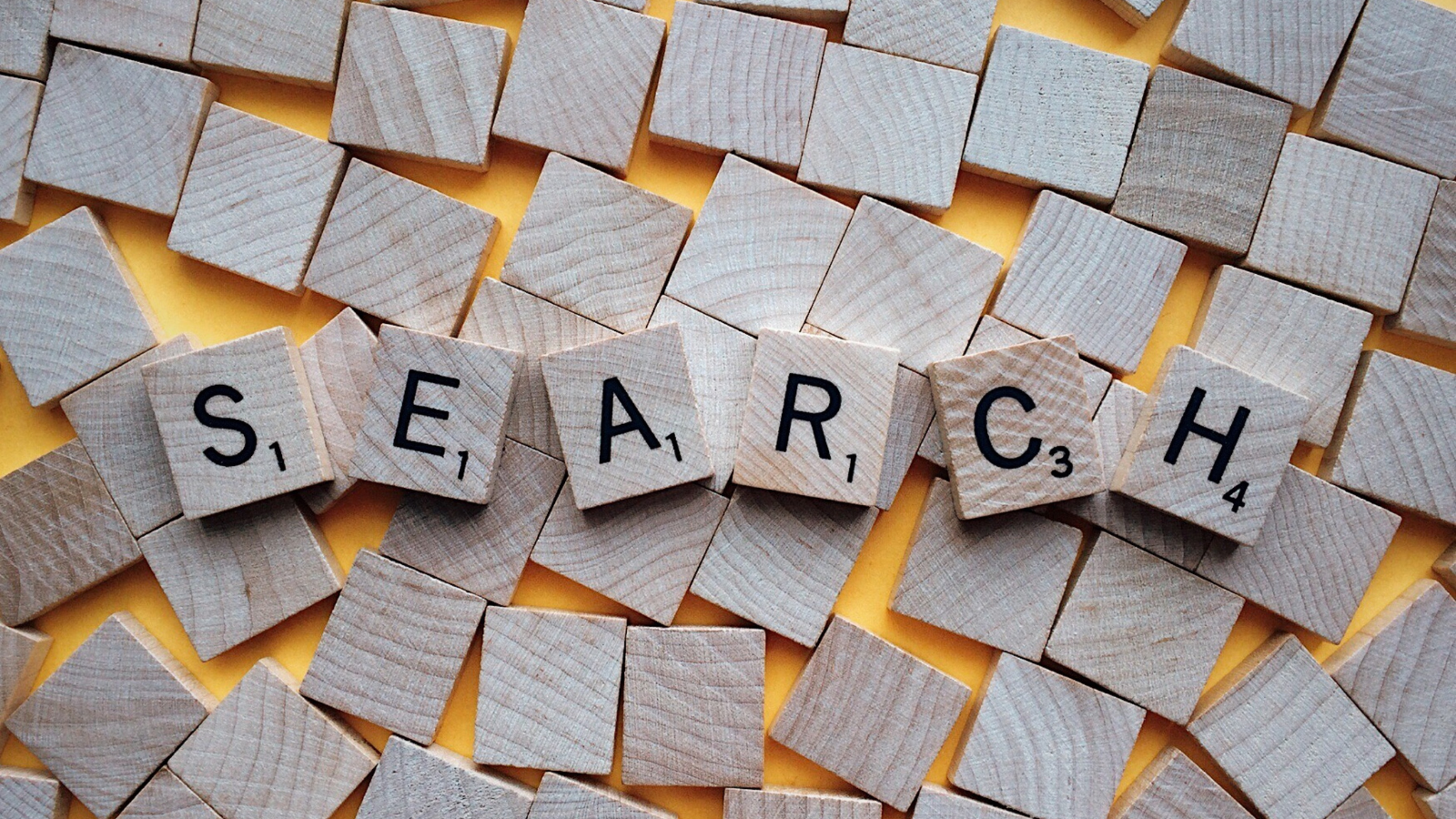 Scrabble tiles spelling "SEARCH" lay across a yellow background.