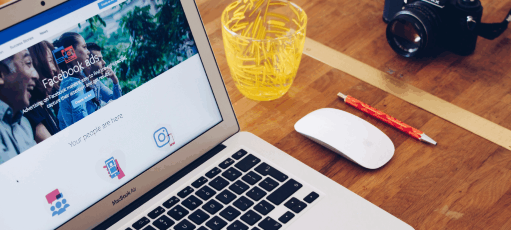 A work laptop sits on a wooden desk with Facebook Meta Ads showing.