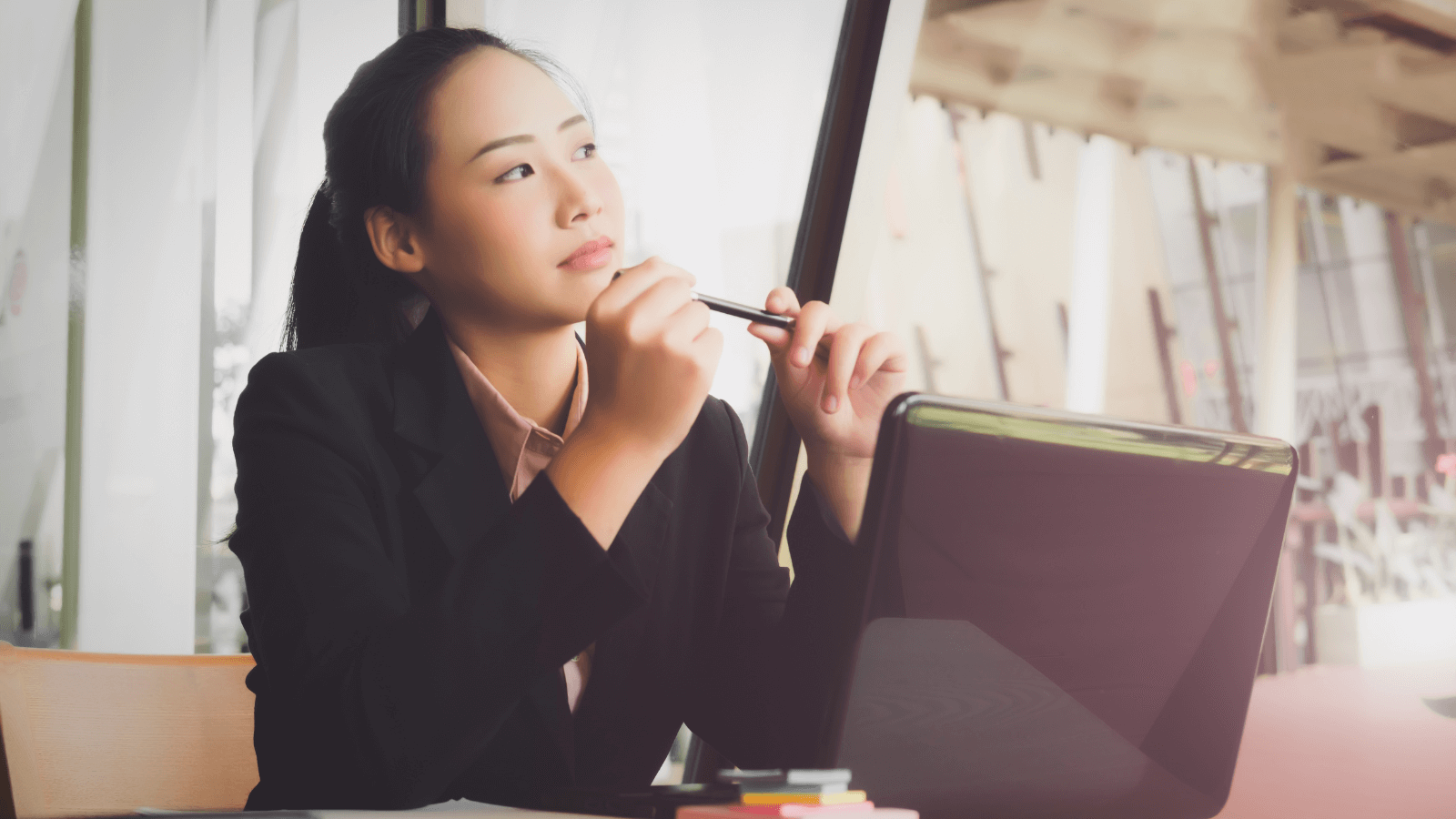 A woman sits thinking next to a laptop.