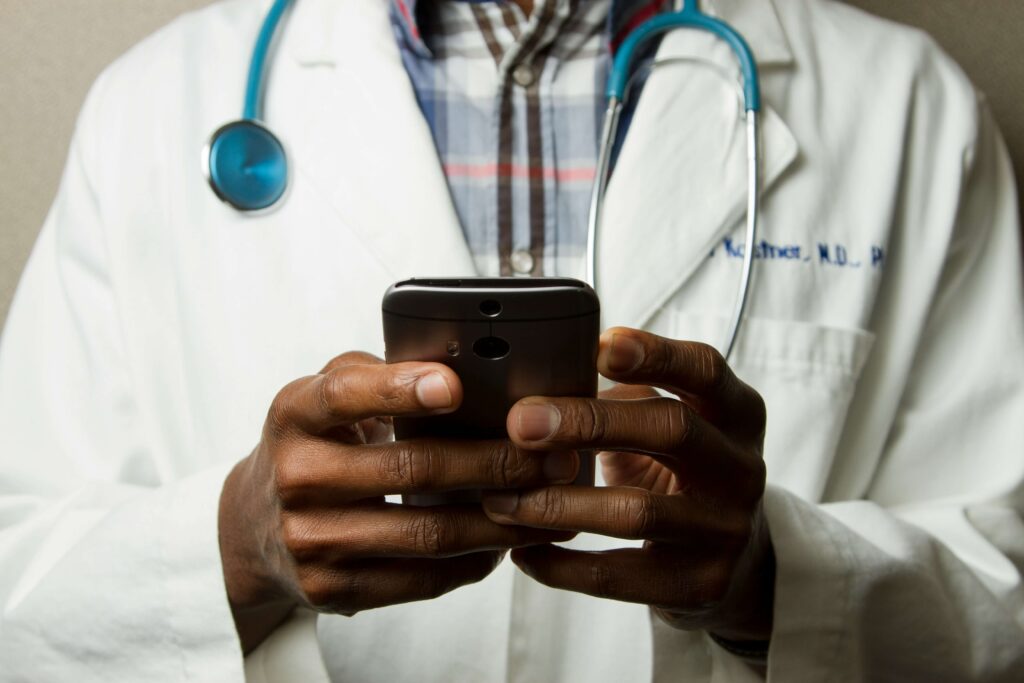 A doctor wearing a lavatory gown and stethoscope uses a cell phone. Represents concept of finding a healthcare marketing agency. Image credit: National Cancer Institute from Unsplash.