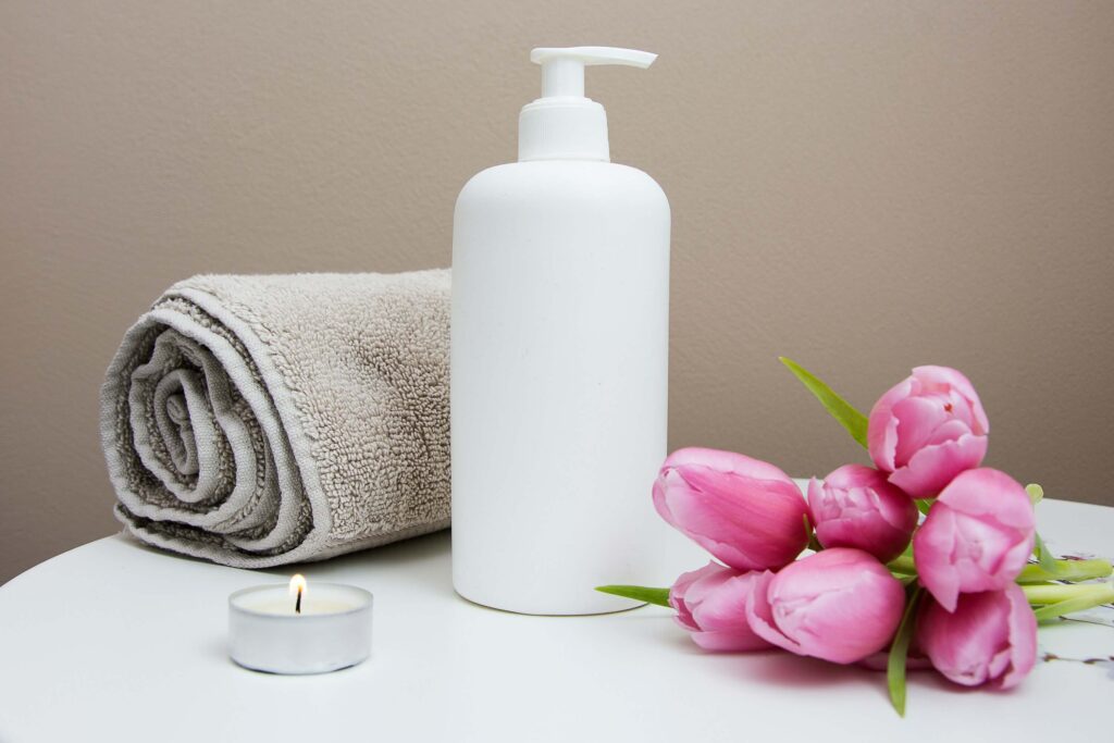 White plastic pump bottle next to a gray towel, tea candle, and pink tulips on a table at a med spa. Image credit to Camille Brodard from Unsplash.