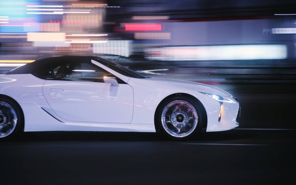 A white sports car races in front of city lights. Photo by Takashi Miyazaki on Unsplash.