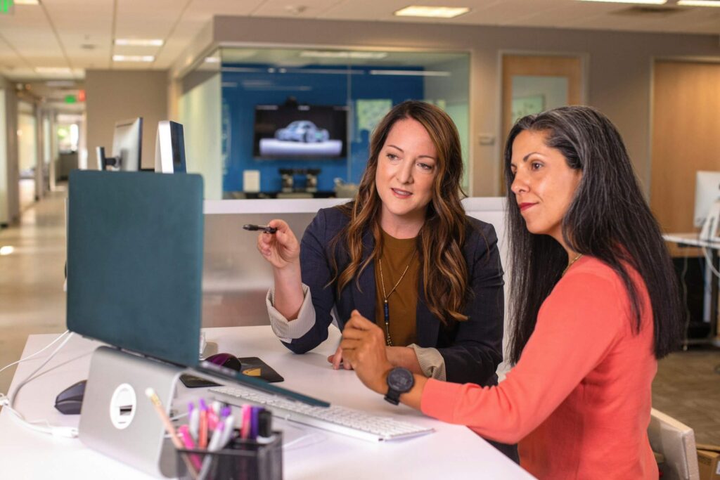 Two business women talking about sales in an office, at a desk with a laptop, representing the concept of professional services marketing agencies. Photo courtesy of LinkedIn Sales Solutions (linkedinsalesnavigator) on Unsplash.